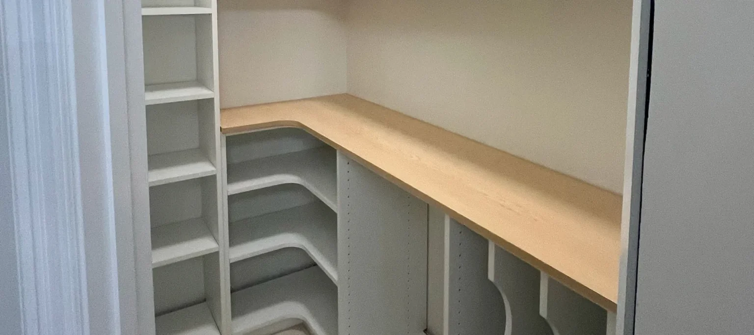 Custom walk-in pantry with white corner shelving and a light wood countertop