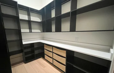 Walk-in pantry with black shelving, a white countertop and wood drawers
