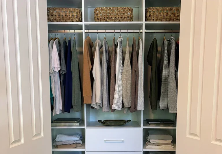 Reach-in closet behind double doors with lighted hanging rods, baskets and a center drawer