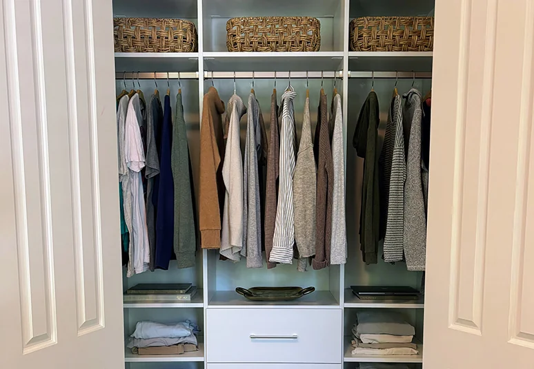 Reach-in closet behind double doors with lighted hanging rods, baskets and a center drawer